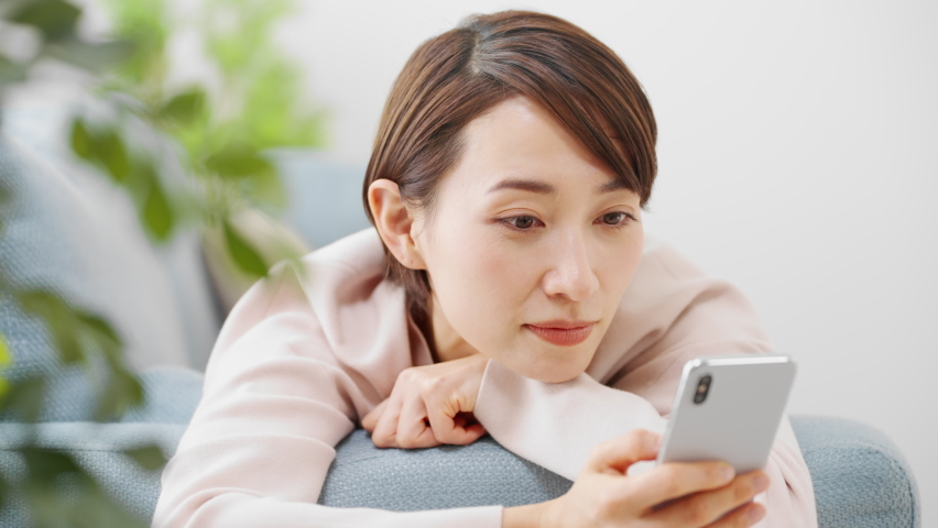 A young woman using a smartphone while sitting on a sofa.