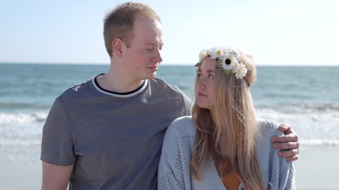 Man hugging his wife in a beautiful flower crown on a sunny summer day. Portrait of lovely couple smiling on a sandy beach along ocean coastline. High quality 4k footage
