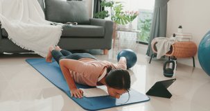 Young attractive Asia woman in sportswear watching fitness online video on tablet practice yoga for beginner in living room at house. Home quarantine workout and fitness exercise without the gym.