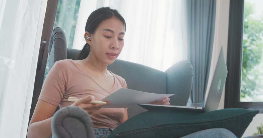 Asia businesswoman using laptop talk to colleagues about plan in video call while working from house at living room. Remotely at workplace, social distancing, quarantine for corona virus prevention. | Shutterstock HD Video #1091631579