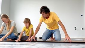 A family of mother, father and son install laminate on the floor in their apartment. DIY concept. Slowmotion video