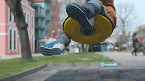 Little cheerful boy in blue hat and warm clothes spends his free time on bright playground in kindergarten in autumn empty park, and rides on blue modern swing in cloudy weather. HD slow-motion video