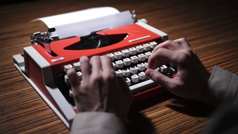 Men's hands press the buttons on a vintage typewriter. Red typewriter. General plan on the table.
