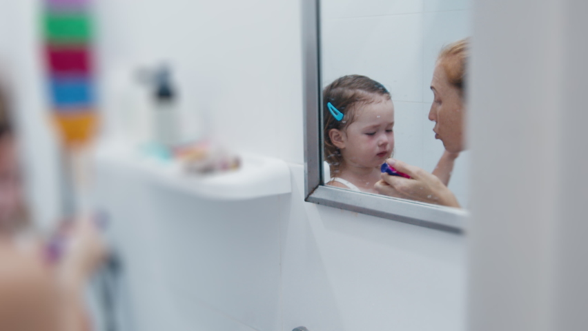 Angry woman talks to the sad toddler girl and brushes the kid's teeth in the bathroom Royalty-Free Stock Footage #1091636411