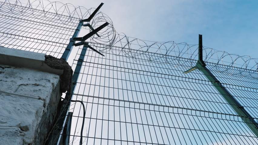 The barbed wire of the correctional facility on the background of a gloomy cloudy sky. Fence on the border of two states, protecting from illegal migrants and refugees Royalty-Free Stock Footage #1091636671