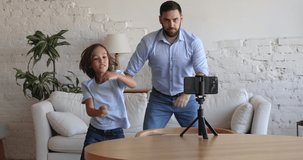 Happy energetic dancers, bloggers, dad and son kid dancing to music at smartphone frontal camera, recording self video, jumping, smiling, having fun. Active father and boy exercising at home