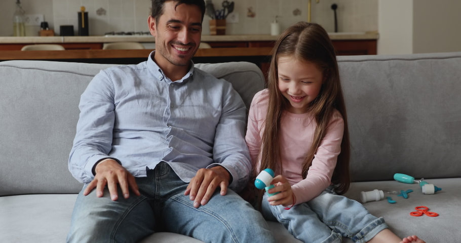 Happy cute little girl playing nervous system doctor, knocking on fathers joints with medical hammer, examining knee, fingers, giggling, laughing. Dad enjoying game with daughter, pretending patient Royalty-Free Stock Footage #1091638923