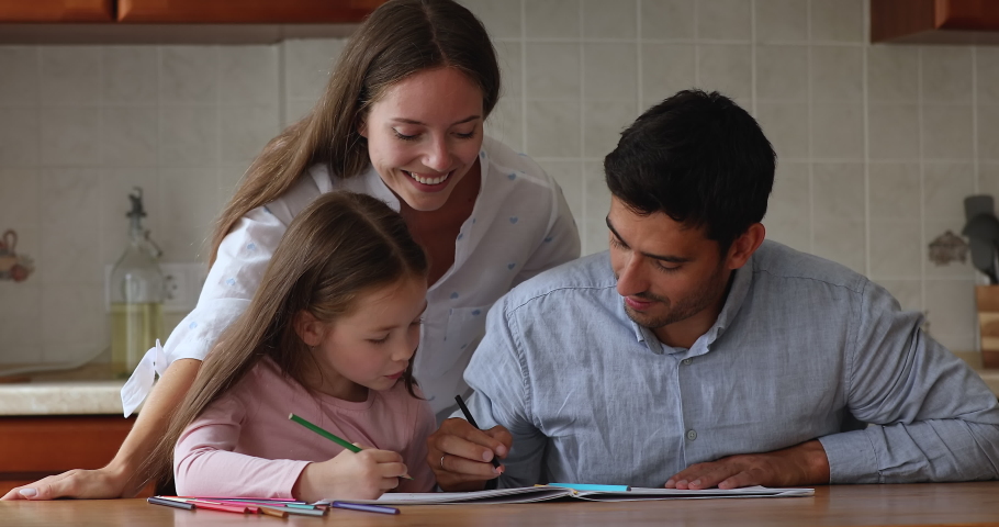 Happy loving mom watching handsome dad and little daughter kid doing primary school homework together, writing letters, drawing doodles in paper album. Father helping kid with study home task | Shutterstock HD Video #1091638963