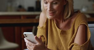 Happy senior mature smartphone user lady enjoying online chat, using virtual app on mobile phone, touching screen, reading text message, watching internet content, smiling, laughing
