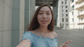 shot of young asian girl making online video call talking looking at camera outdoors holding gadget with camera standing in the street.