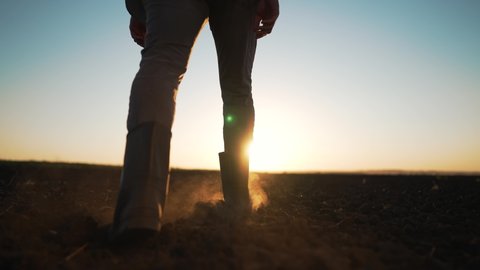 Agriculture. farmer at sunset walk on fertile soil. Farm worker silhouette. The foot of a man in rubber boots walk through the mud. Farmer agronomist works on land plot at sunset. Agriculture concept