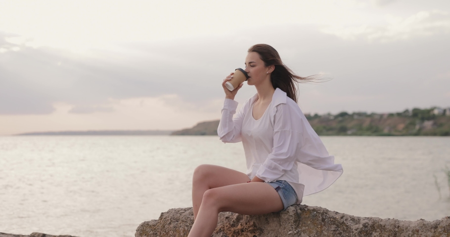 Young woman drinking takeaway coffee near the sea, slow motion