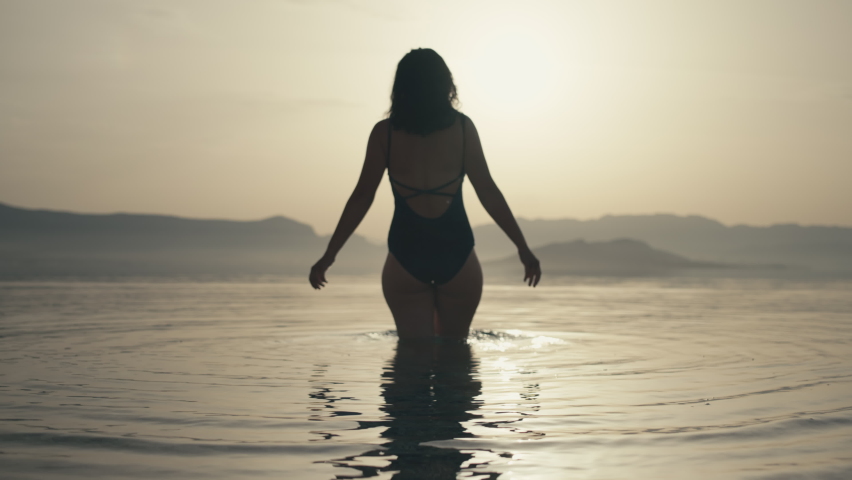 Slow motion video of a girl diving into the sea at sunset in a beautiful landscape. A woman in a bathing suit goes swimming in the ocean. Royalty-Free Stock Footage #1091650713