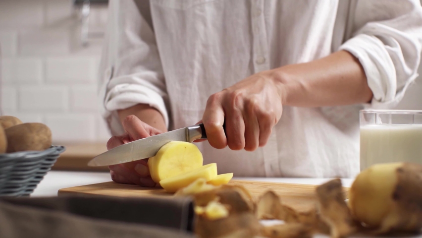 Cook, wife, mother. Cooking lunch, dinner in kitchen. Cutting vegetables, potatoes on wooden board. Woman cuts potatoes on cutting board. Hands cutting potatoes on bamboo cutting board. Potato milk
 Royalty-Free Stock Footage #1091652039