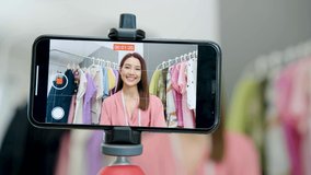 Young asian woman business owner at fashion store using smartphone live streaming for sale fashion clothing to customer and present detail on social media, online market delivery concept.