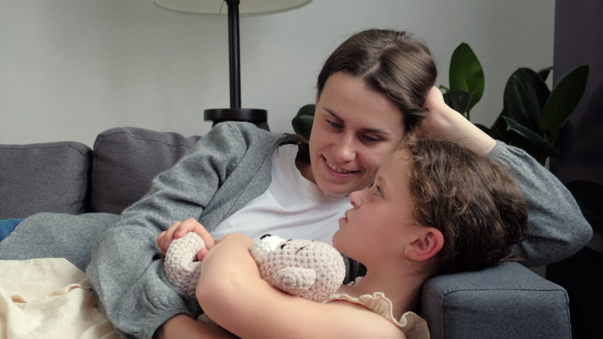 Close-up of loving mother cuddles and talking with little daughter lying on cozy sofa, feel unconditional love show devotion, express caress. Caring mom, adopted kid, Mothers Day celebration concept Royalty-Free Stock Footage #1091660917