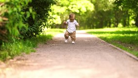 the first steps of the baby, the child walks along the path summer in the park, a one-year-old child walks independently, slow motion video