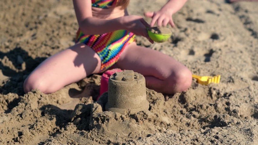 Little girl playing with sand on beach ocean sea. Childhood and summer vacation concept. Smiling child having fun outdoors on family holidays. Kid building sand castle. Trip to warm countries | Shutterstock HD Video #1091666017