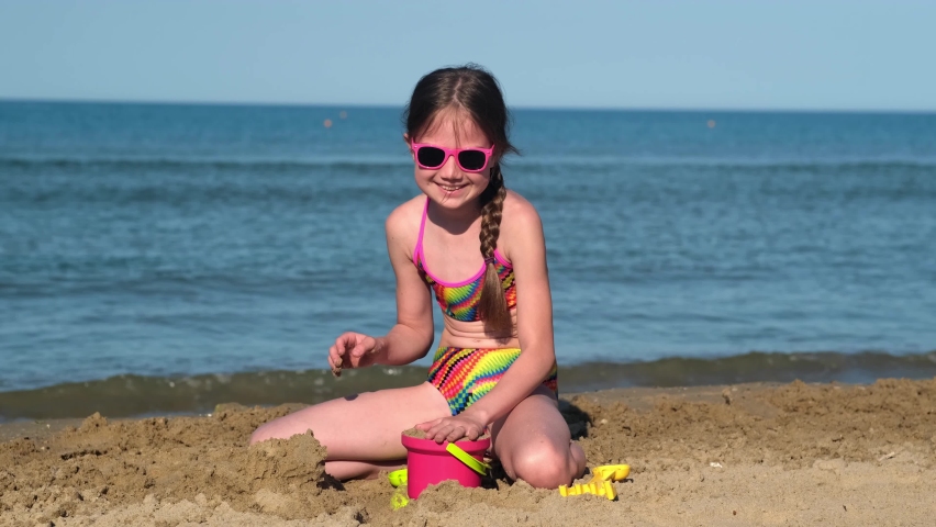 Cute little girl playing with sand on beach ocean sea. Childhood and summer vacation concept. Smiling child having fun outdoors on family holidays. Kid building sand castle. Trip to warm countries | Shutterstock HD Video #1091666019