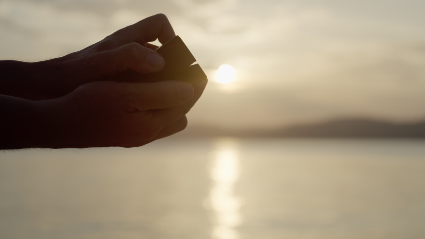 Close-up of guys opening a box with a hoop by the sea at sunset. Proposal to marry in a beautiful place and happy people together.