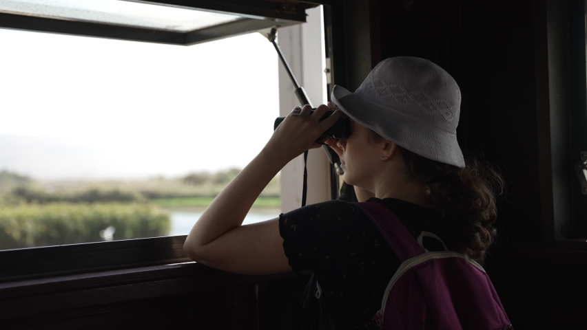 Woman birdwatcher observing birds from observation station in natural reserve. Female using binoculars for spotting rare birds in their natural habitat and environment. Standing at window and looking | Shutterstock HD Video #1091671321