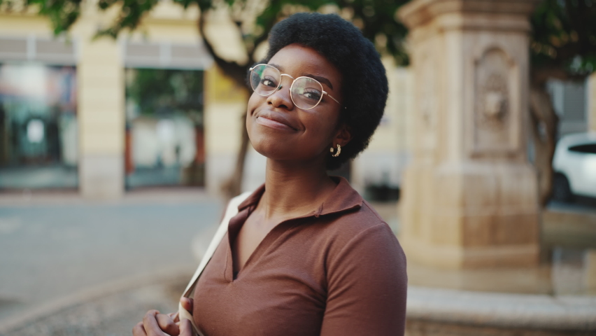 Beautiful African woman in glasses looking charming posing at camera on the street. Carefree curly girl looking happy outdoors