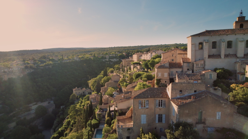 Aerial view of the village of Gordes, in the south of France. Small medieval tourist village at the top of a hill during sunset with forest and a blue sky on the horizon. | Shutterstock HD Video #1091681085