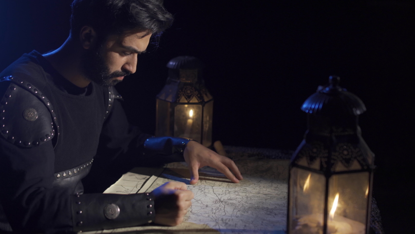 The commander who found the right tactic on the map.
War preparation in historical times. Armored, protective clothing. Cloak. Map and chess pieces standing on it. Candlelight and arrow. 