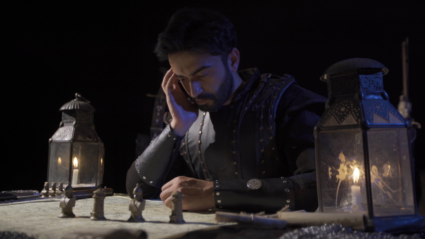 The commander who got angry and knocked on the table while planning.
War preparation in historical times. Armored, protective clothing. Cloak. Map and chess pieces standing on it. 