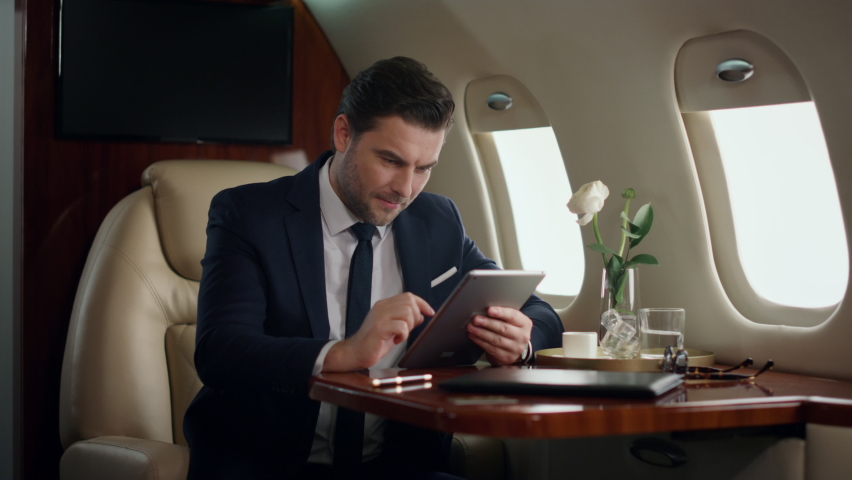 Stressed businessman working tablet in airplane. Professional touch pad screen checking company reports. Serious stylish ceo browsing web on business trip. Thinking man using digital computer in jet | Shutterstock HD Video #1091685177