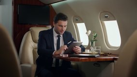 Stressed businessman working tablet in airplane. Professional touch pad screen checking company reports. Serious stylish ceo browsing web on business trip. Thinking man using digital computer in jet - Powered by Shutterstock - Get 15% off with code: PIKWIZARD15