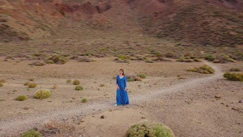 Woman in a blue dress in the middle of a landscape of hardened lava in the Teide National Park. Drone flying around a person
