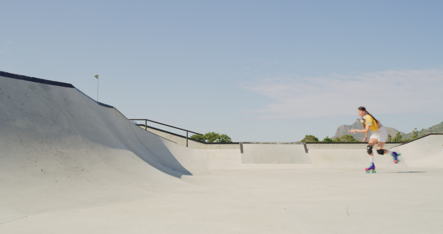 A young female and male roller skater jumping and skating on a ramp at the skatepark outside. Two skilled friends riding and practicing their rollerblading tricks or technique for a competition