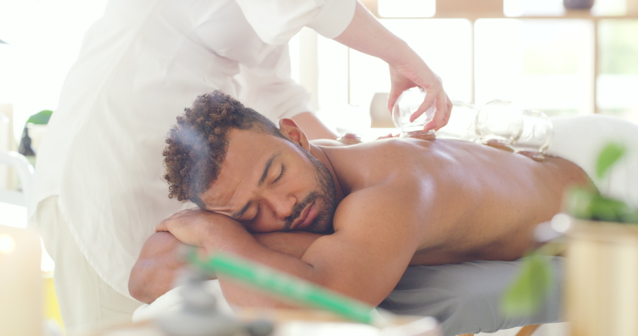 Young man enjoying relaxing and therapeutic back massage treatment with vacuum cups in a spa. Beauty therapist treating muscle pain with suction cupping therapy to remove body toxins Royalty-Free Stock Footage #1091689035