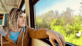 Young relaxed man riding on train. Dreamy guy with blonde dreadlocks looking at nature through window. Thoughtful male passenger sitting in suburban train. - Powered by Shutterstock - Get 15% off with code: PIKWIZARD15