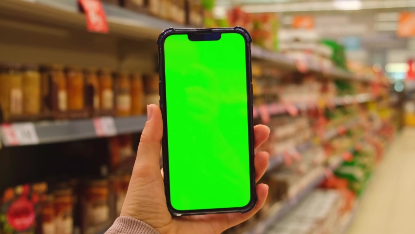 4k Mobile phone Chroma key for mobile app application. Close up of woman hand holds smart phone with green screen at shopping mall store. Buying food at supermarket, grocery shop center online
