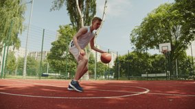 Teenager dribbling on an outdoor court, during a bright and sunny summer day. Video of a white caucasian teen training to play basketball. Video of a male doing basketball tricks. 
