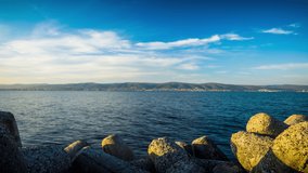 A small concrete reliable breakwater against the background of a spacious blue cloudy sky and a raging blue empty Black Sea, with white sea strong waves. 8K UHD timelapse video