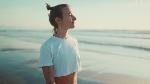 Attractive blond woman looking happy breathing fresh air during walk along the sea after yoga practice. Sporty girl enjoying morning on the beach