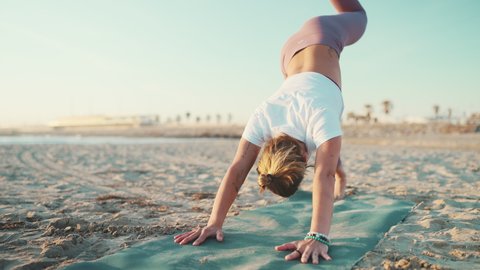 Sporty woman doing warmup exercise on yoga mat outdoors. Young yoga teacher stretching during yoga practice on the beach
