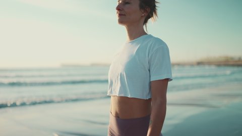 Tracking shot of beautiful woman breathing fresh air during walk along the sea. Sporty girl with slim body enjoying morning on the beach