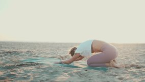 Attractive woman doing yoga exercises outdoors. Young yogi woman exercising on mat stretching body at the beach. Morning yoga