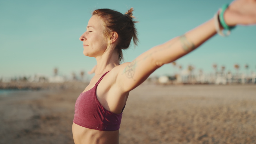 Portrait of beautiful blond woman enjoying morning yoga practice on the beach. Sporty tattooed girl stretching before workout by the sea | Shutterstock HD Video #1091692509