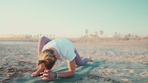 Beautiful healthy woman on mat doing warmup exercise. Young yoga teacher stretching during yoga practice on the beach