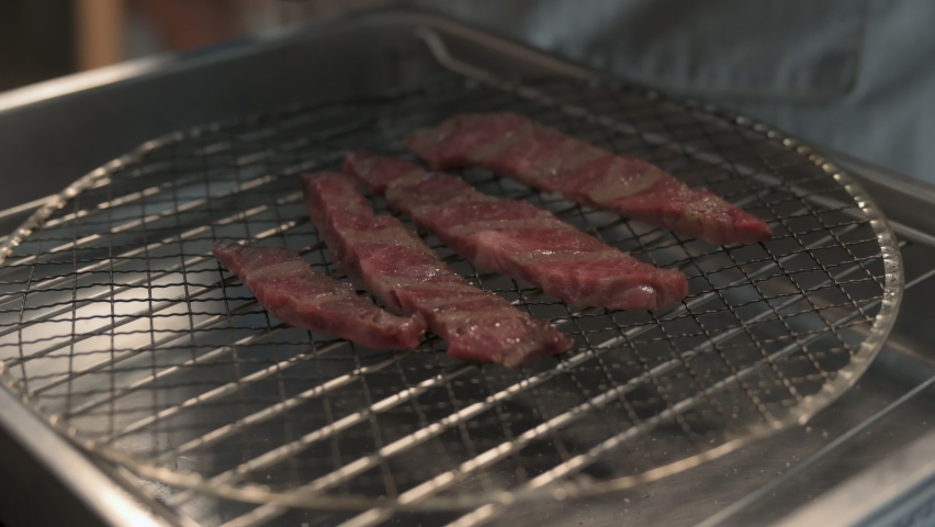 Chef Grilled Wagyu beef.,Juicy beef steak is fried on fire coals on iron grill on dark background in flame of smoke. Royalty-Free Stock Footage #1091702259