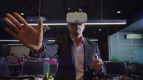 A moving shot of an Indian Asian corporate male or. man wearing VR or Virtual reality headsets or glasses and making hand gestures working on 3D Commercial designs or digital models in a modern office - Powered by Shutterstock - Get 15% off with code: PIKWIZARD15