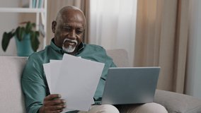 African American businessman elderly 60s bald man sitting at desk typing on laptop manage household paperwork business finances documents managing papers planning budget working in office pay online - Powered by Shutterstock - Get 15% off with code: PIKWIZARD15