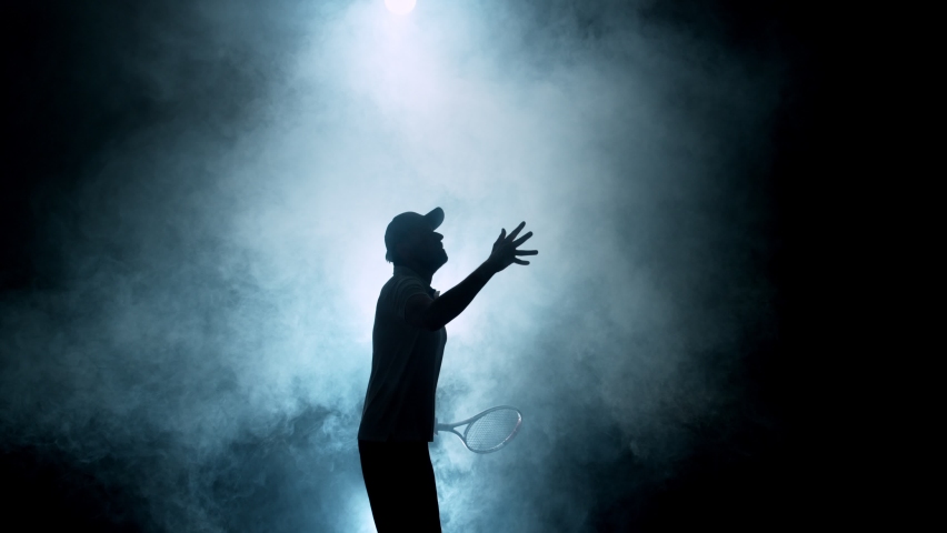 Super slow motion of tennis player silhouette hitting ball. Smoke effect around, black background. Filmed on high speed cinema camera, 1000fps.