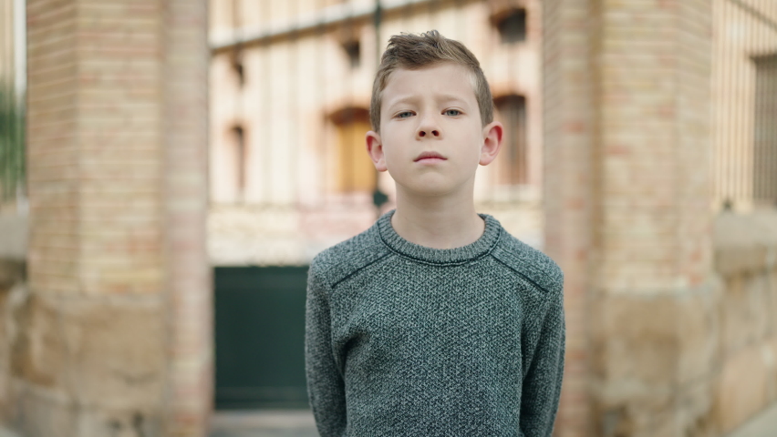 Blond child with relaxed expression doing stop gesture at street