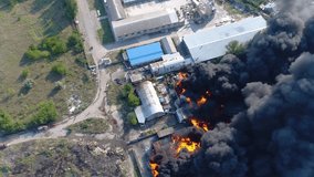 Rocket attack on the plant. Warehouse building strong fire in warehouses black smoke and fire. Shooting from a drone over a large-scale fire. Grain video. Rescuers put out a huge fire
